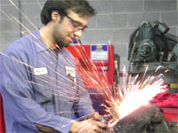 A mechanic grinding a car part while sparks are flying