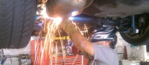 A mechanic welding under a lifted car at a repair service station